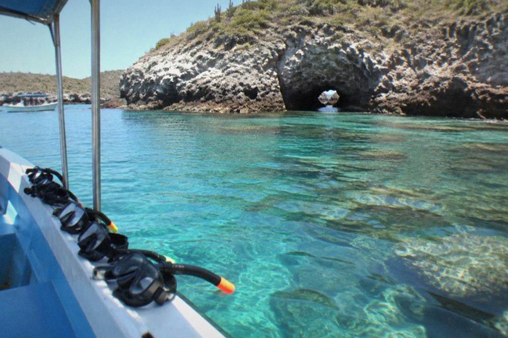 Snorkel boat anchored in clear turquoise water beside a rocky island marine park