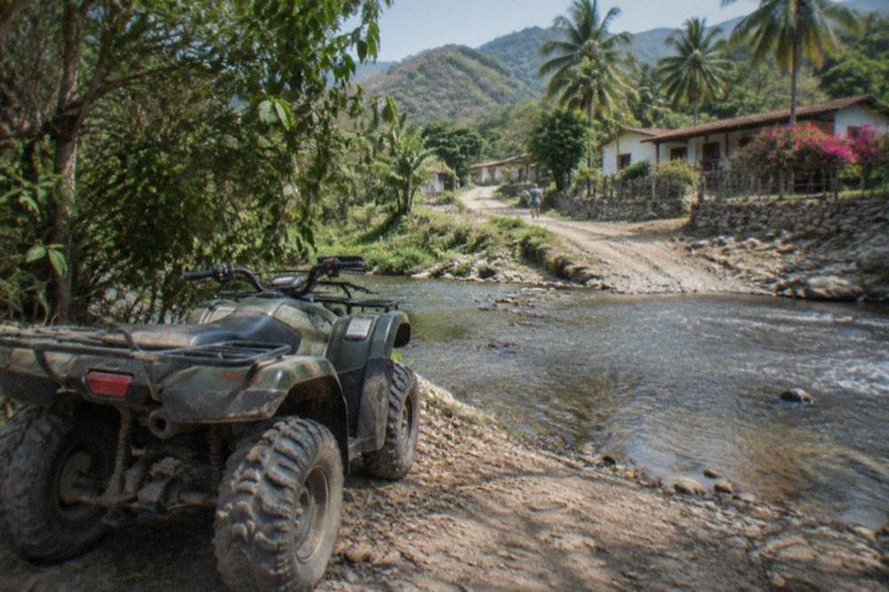 A single ATV parked on a dirt jungle trail beside a river crossing