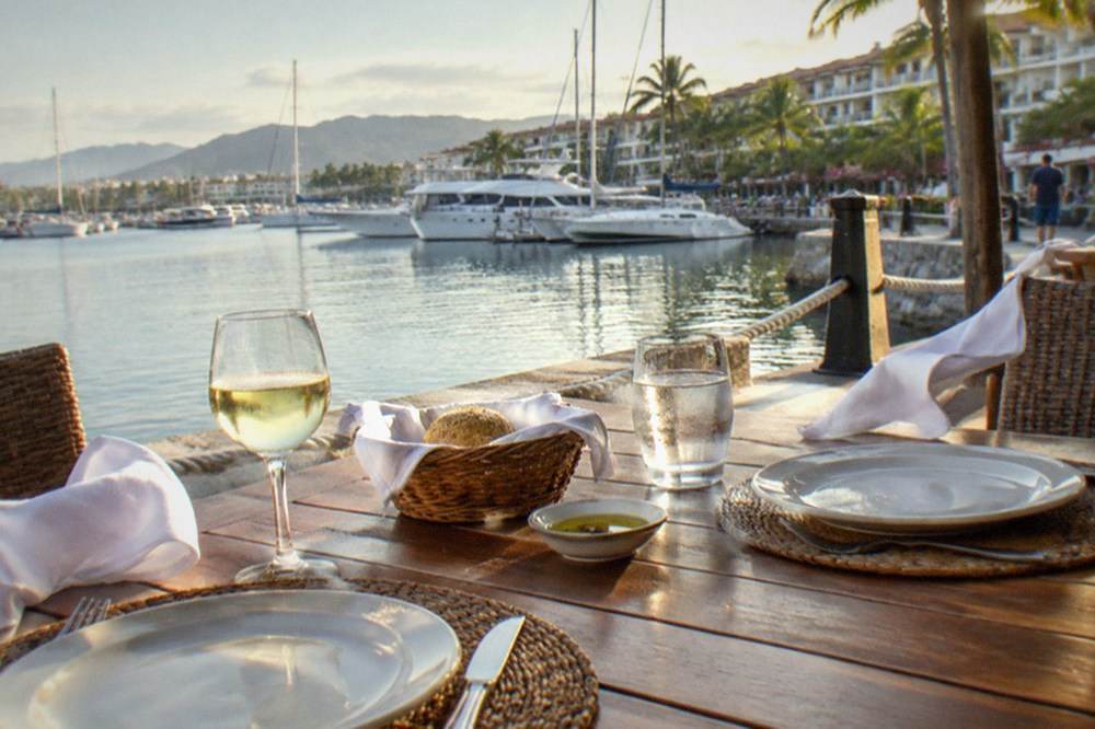 Two place settings on a wooden table at an open-air restaurant overlooking the bay