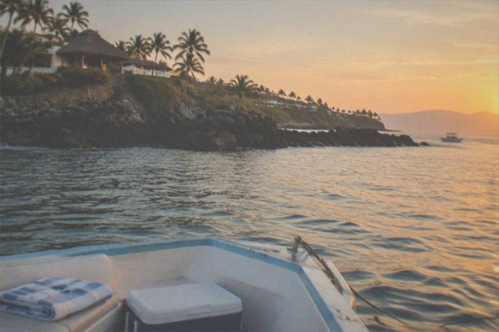A small boat anchored in calm blue water near rocky islands at sunset