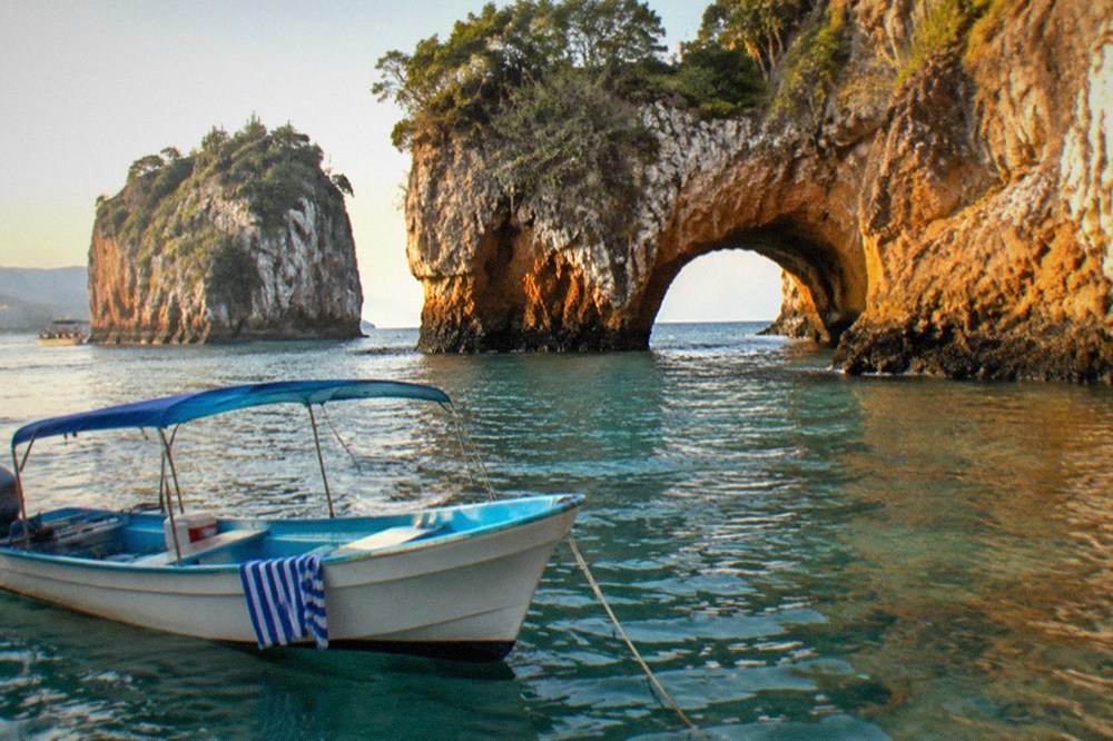 A small boat anchored near tall rocky islands with clear shallow water below