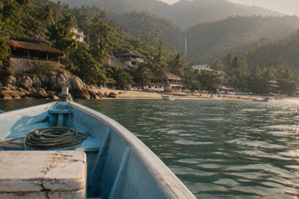 A small fishing boat anchored in a quiet jungle bay with a waterfall visible in the hills behind