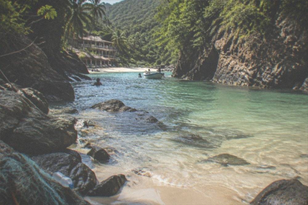 A narrow sandy cove with clear shallow water enclosed by jungle covered rock walls