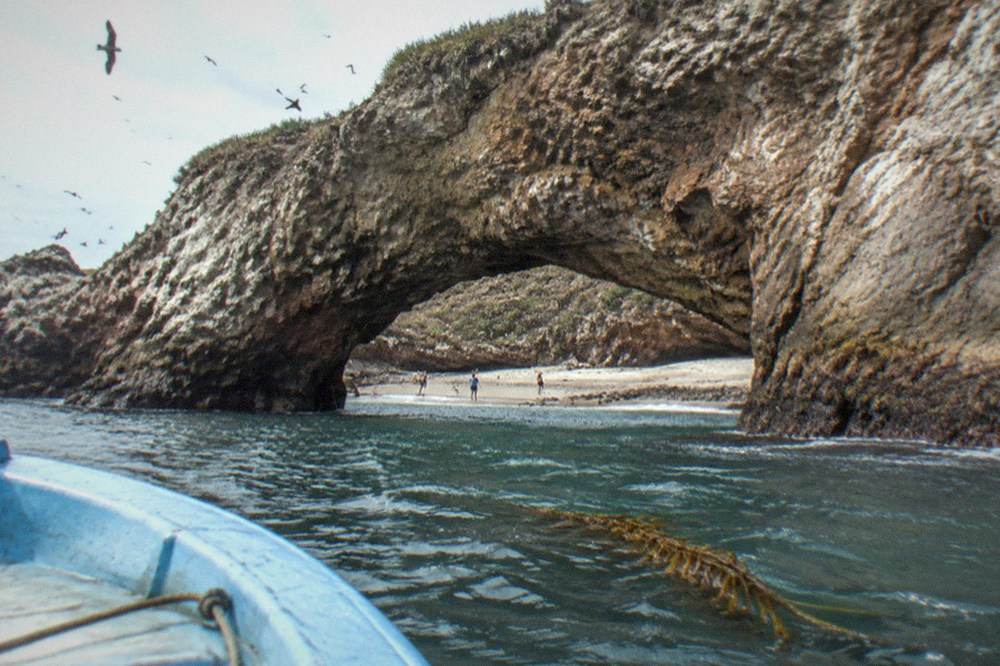 Boat approaching a protected island beach with a natural stone arch