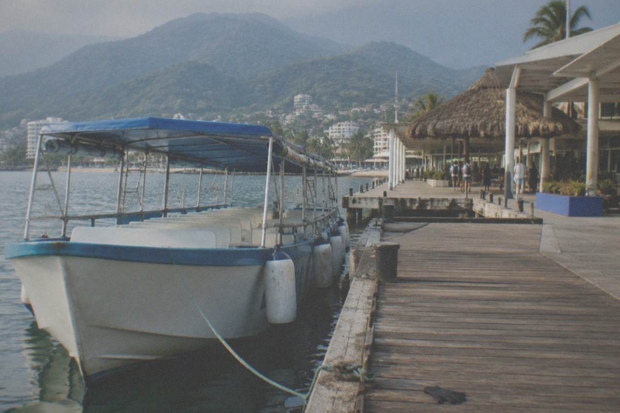 Tour boat moored at a wooden pier in Banderas Bay with jungle-covered hills behind it