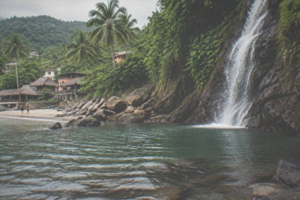Quiet cove with a waterfall meeting the sea and dense green hills behind