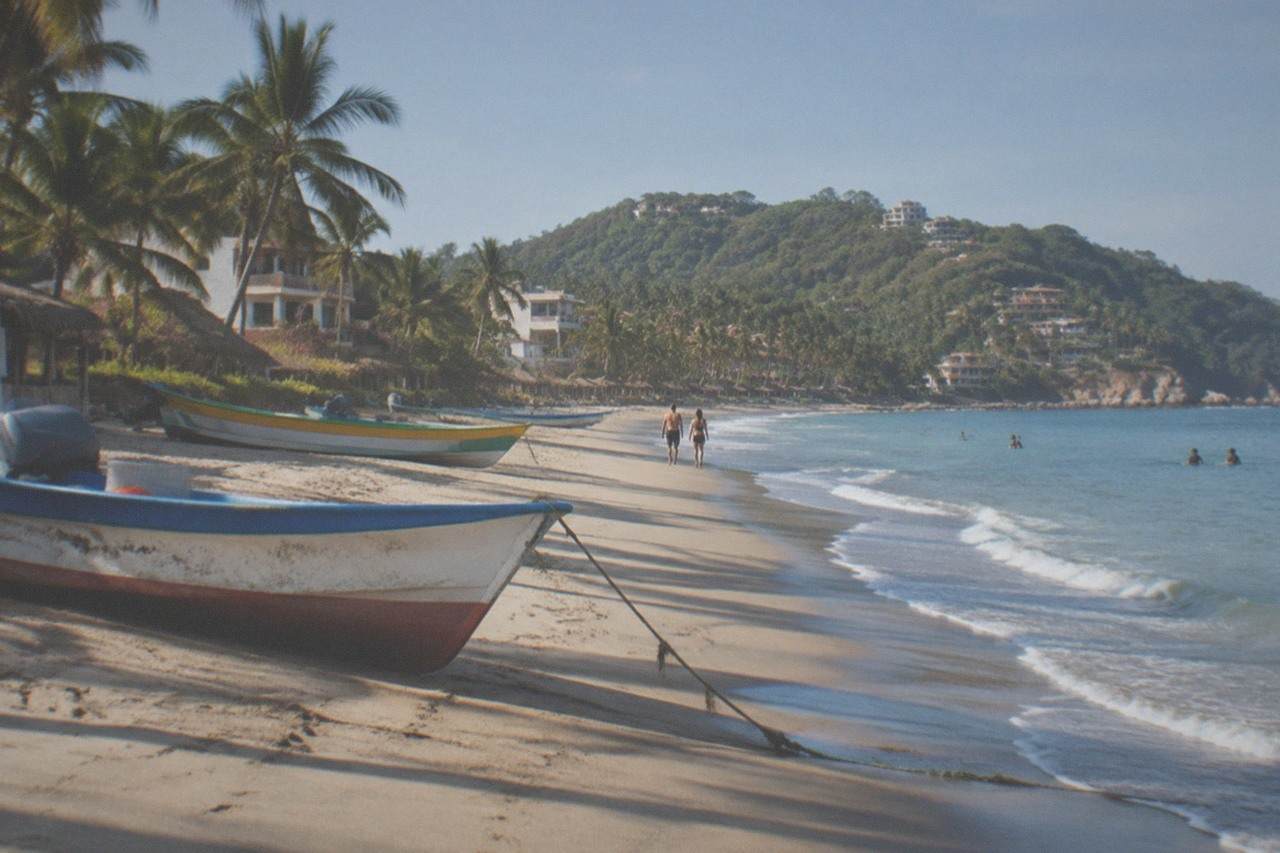 Colorful fishing boats resting on a wide sandy beach beside gentle surf under a bright sky