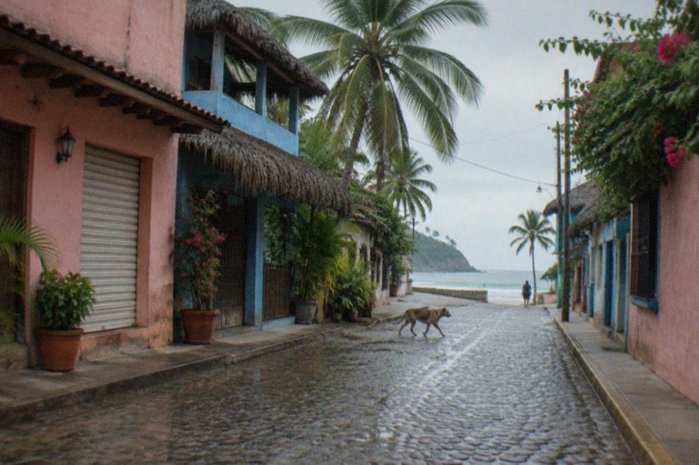 Quiet cobblestone street in a small Mexican surf town with painted buildings and hanging banners