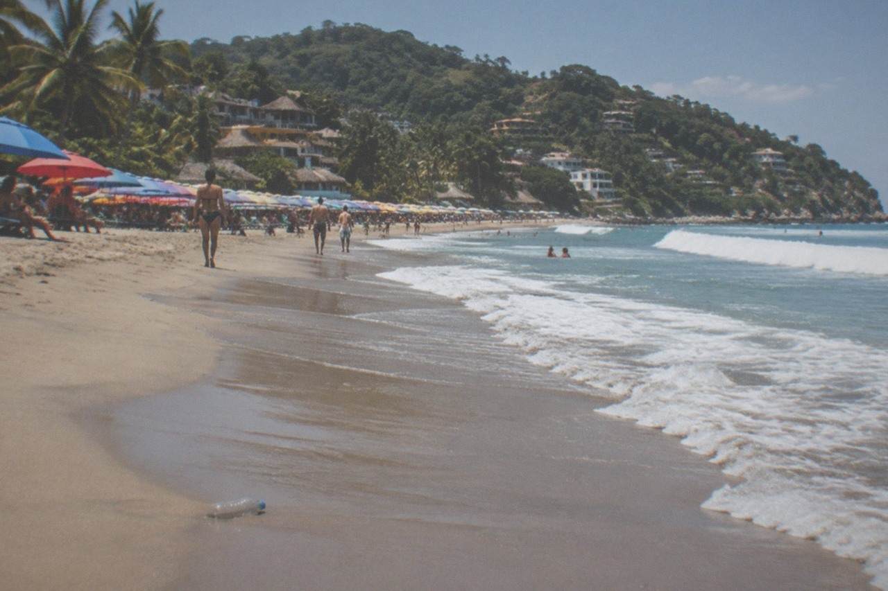 Colorful umbrella rows on a small Pacific beach town shoreline with jungle hills behind