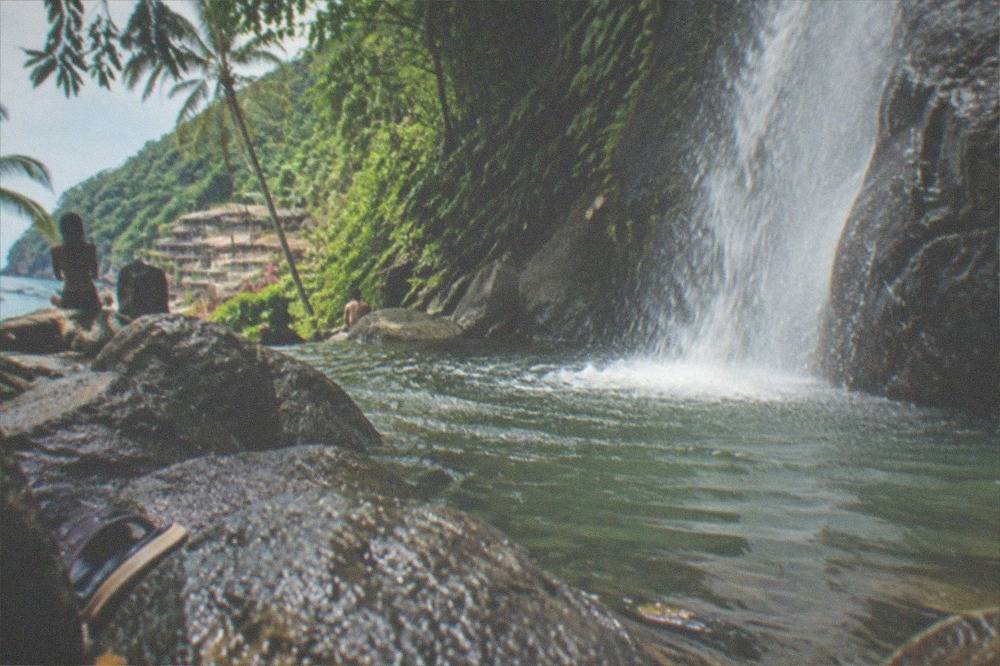 A waterfall dropping through dense green jungle into a rocky pool