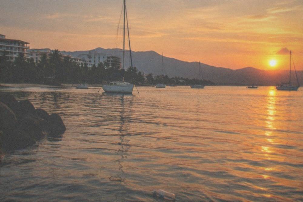 Golden sunset light over calm bay water with boats anchored near a jungle coastline