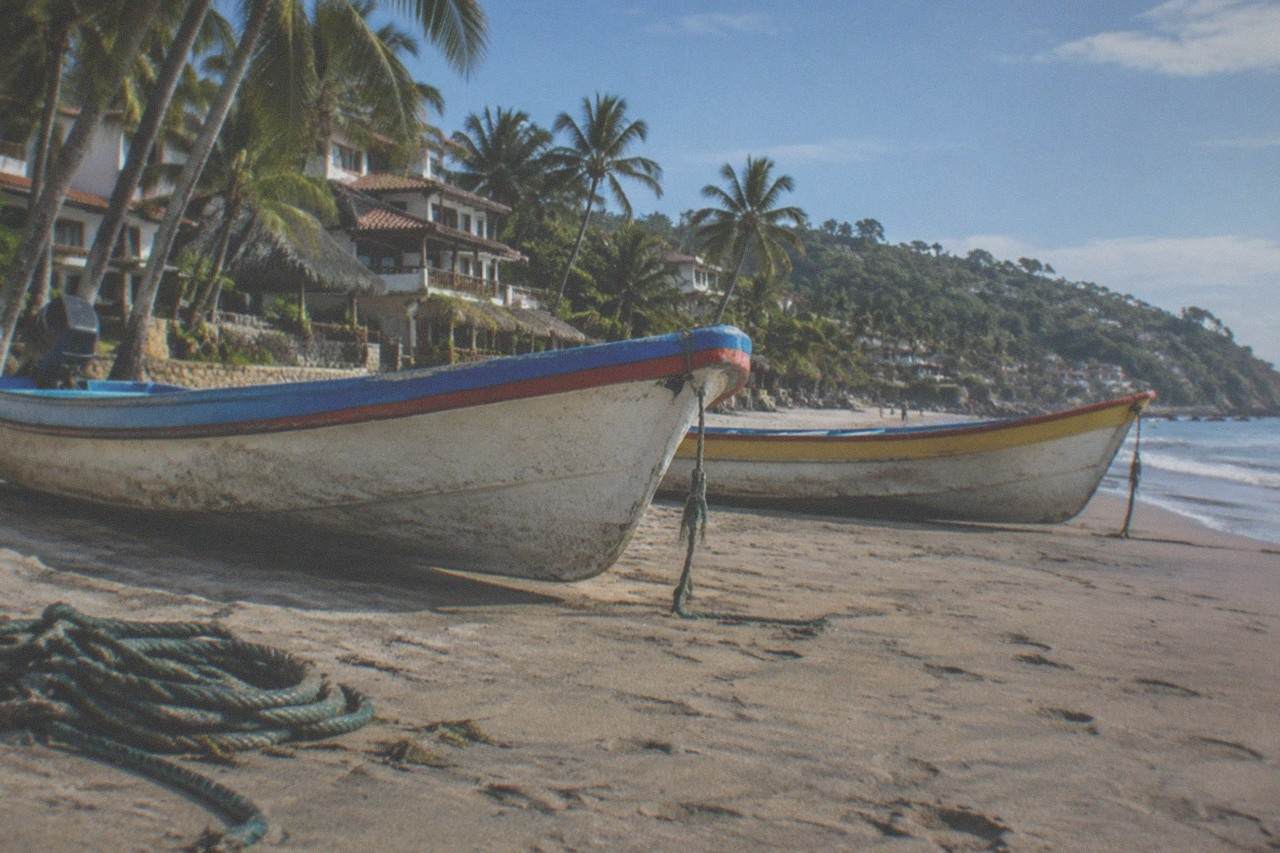Colorful fishing boats resting on a wide sandy beach beside palm trees under a bright sky