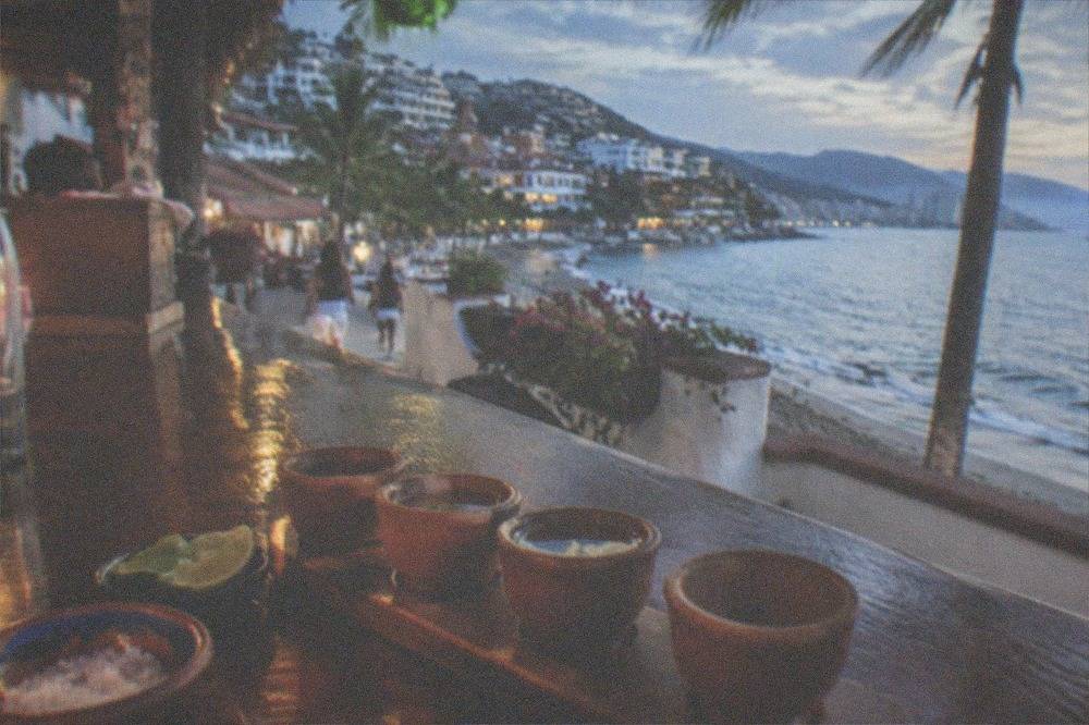 Flight of agave spirits in small tasting glasses beside lime and salt on a wooden bar