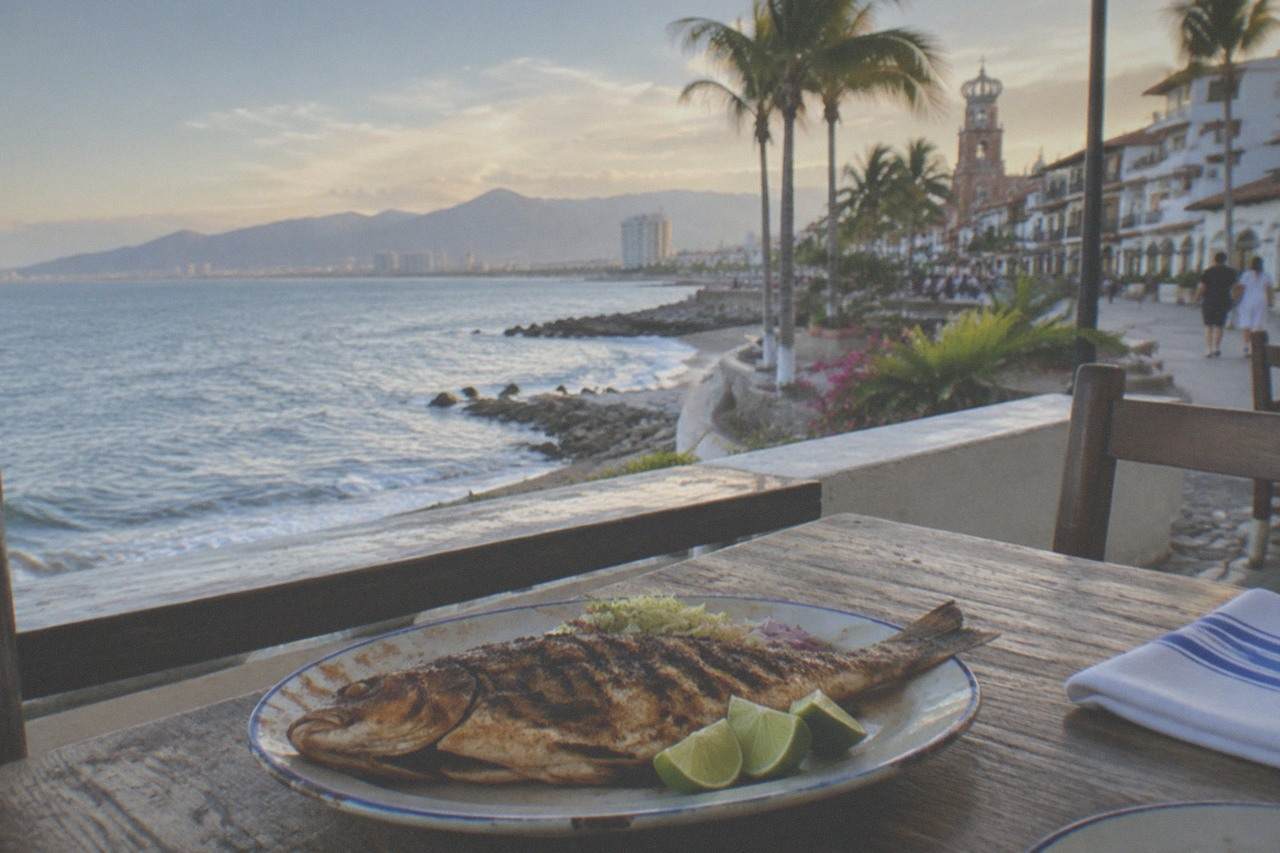 Freshly grilled fish and lime wedges on a beachfront table overlooking the ocean