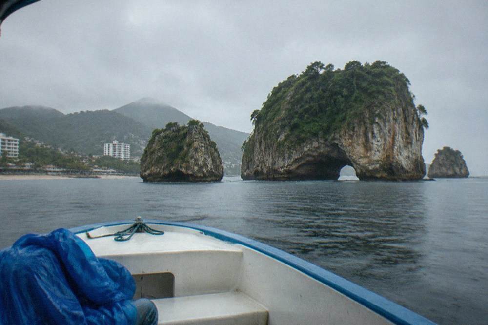 A small boat crossing calm grey water toward rocky islands in the rain