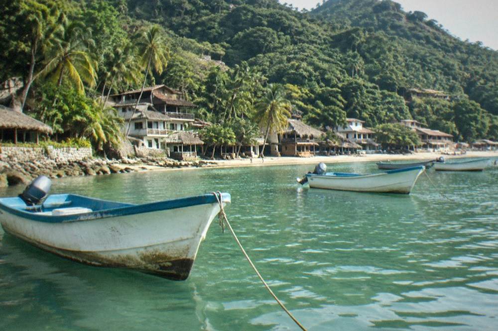 Wooden fishing boats anchored in a calm cove below jungle covered hills