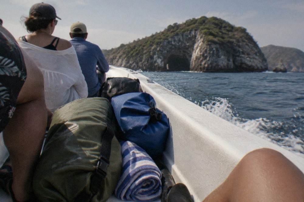 Dry bags and towels packed on the deck of a small boat heading toward island cliffs
