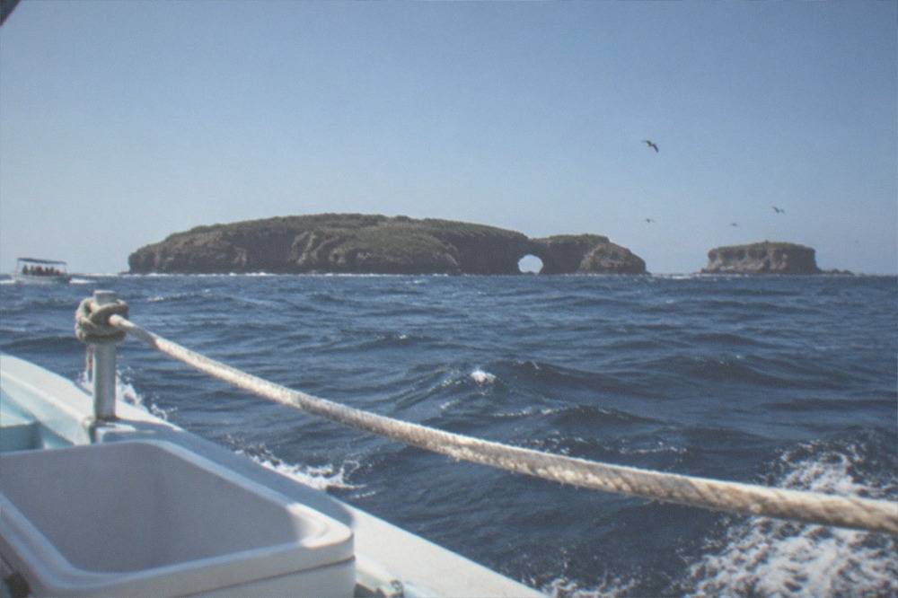 A small boat crossing open blue water toward distant island silhouettes under a clear sky