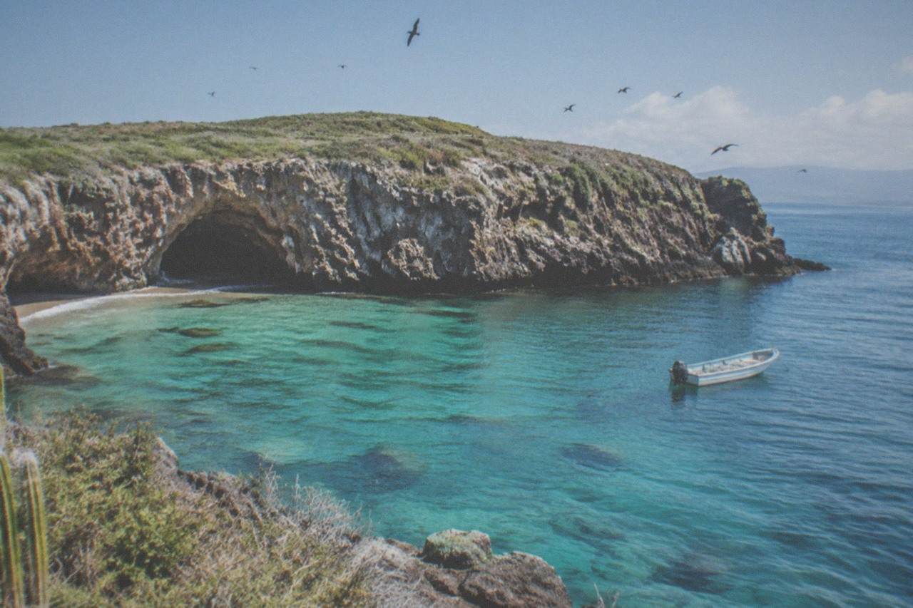 Calm turquoise water around rocky island cliffs with a small anchored boat nearby
