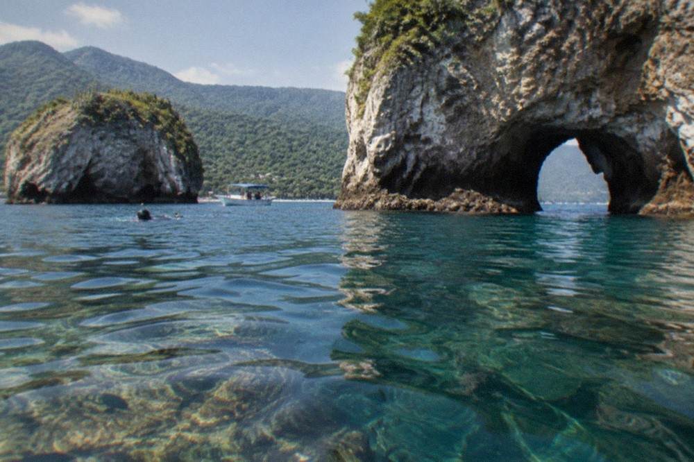 Granite islands of Los Arcos above calm blue water with a rocky reef visible beneath the surface
