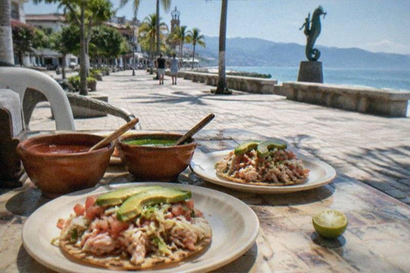 A tasting pour of tequila beside street tacos and salsas at a market stall in downtown Puerto Vallarta.