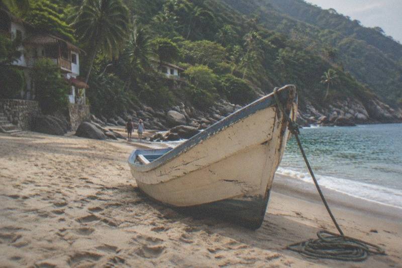 Palapa umbrellas and fishing boats along the shoreline at Yelapa, where steep green slopes meet the calm bay.