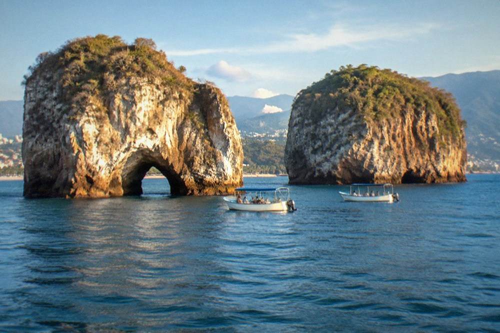 Granite rock islands rising from calm blue ocean with small tour boats anchored nearby