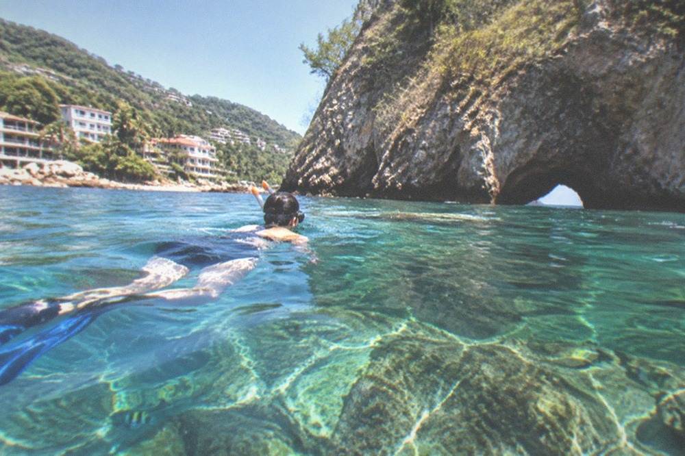 Snorkeler floating above clear water with rocky reef and small tropical fish below the surface