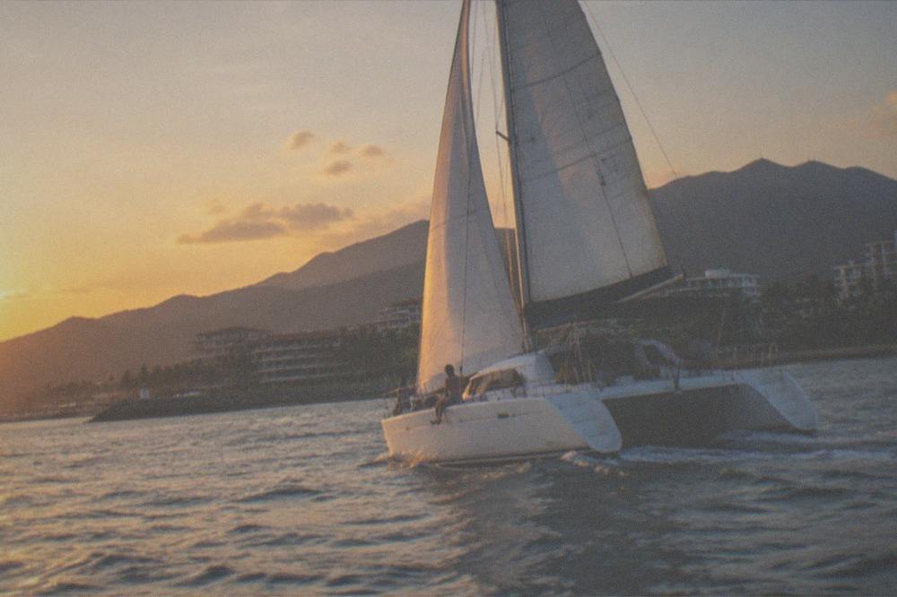 Catamaran with passengers sailing across open bay water toward green coastline at golden hour