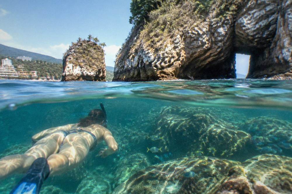 Snorkeler floating above a rocky reef with small fish in clear blue water
