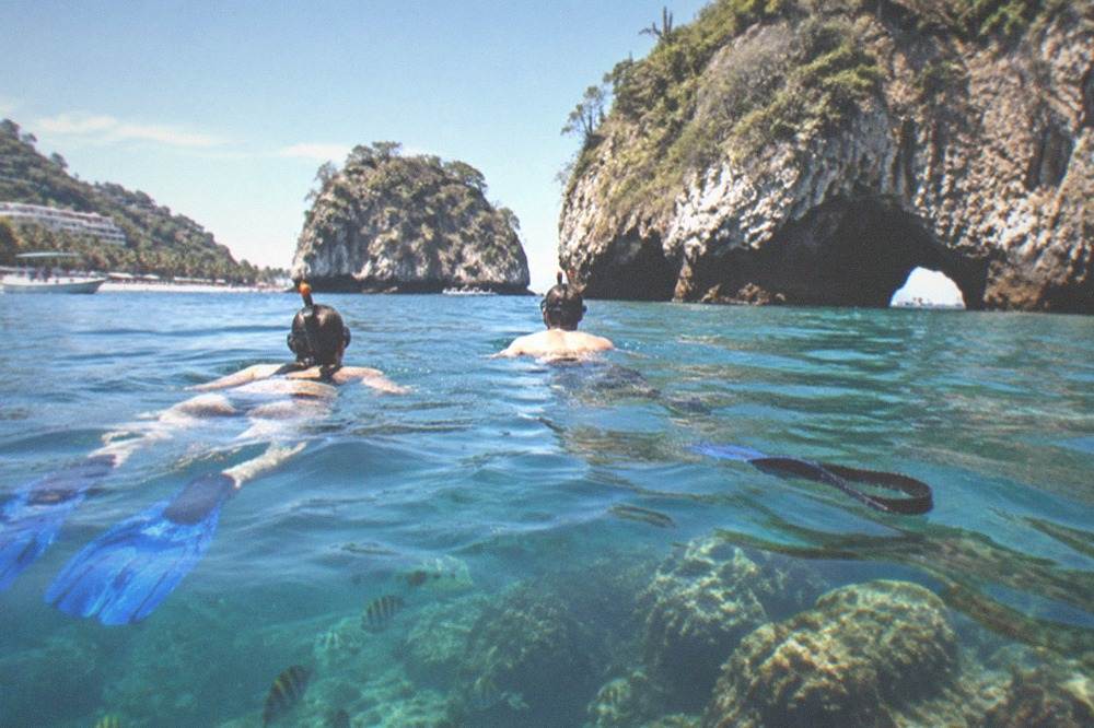 Snorkelers in clear water above a rocky reef near Los Arcos