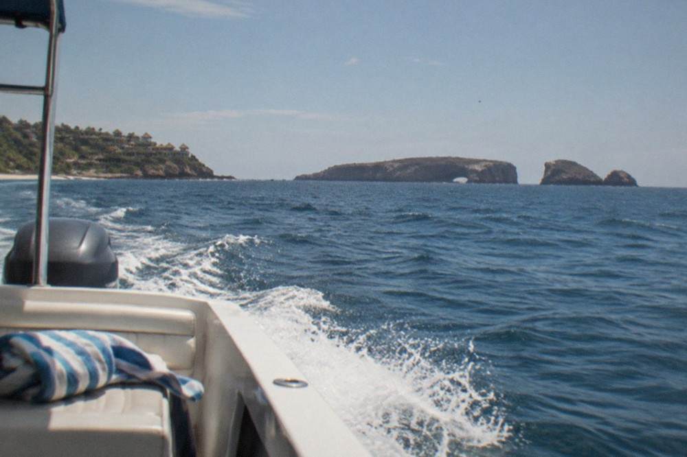 Tour boat cutting across open blue water toward rocky islands on the horizon