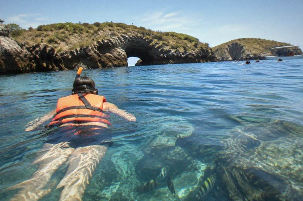 Snorkeler wearing an orange life jacket floating above a coral reef in clear water