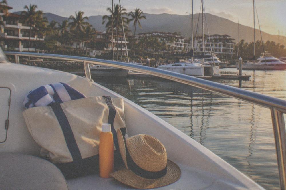 Beach bag with towel, sunscreen and hat on a boat deck with ocean in the background
