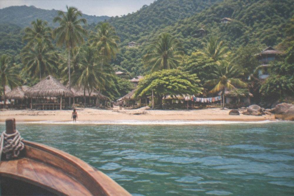 Wooden water taxi approaching a beach village backed by jungle hills