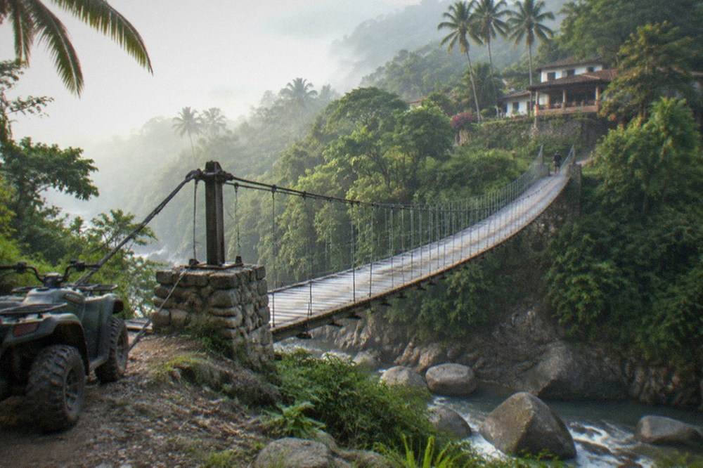 Suspension bridge spanning a jungle river canyon with mist in the valley