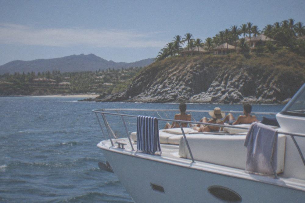 White yacht anchored near a rocky island with guests on deck in bright morning light