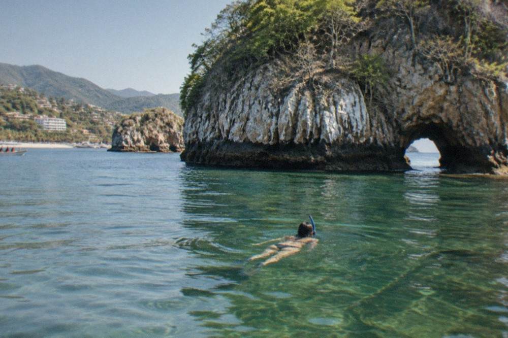 Snorkeler floating above a rocky reef in clear green water