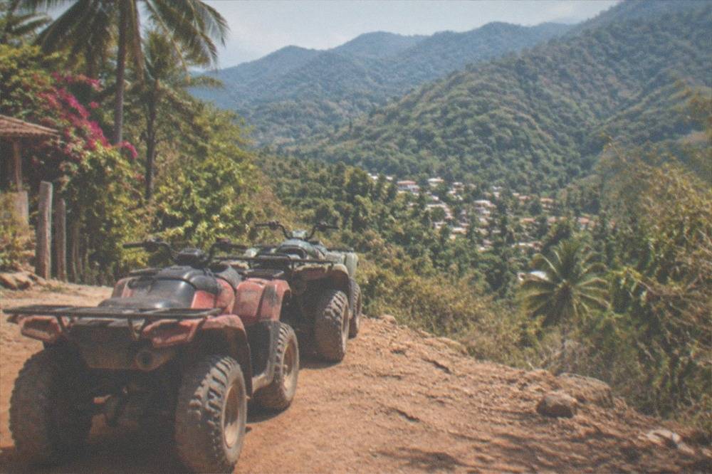 ATVs parked on a red dirt jungle trail with dense green mountains behind them