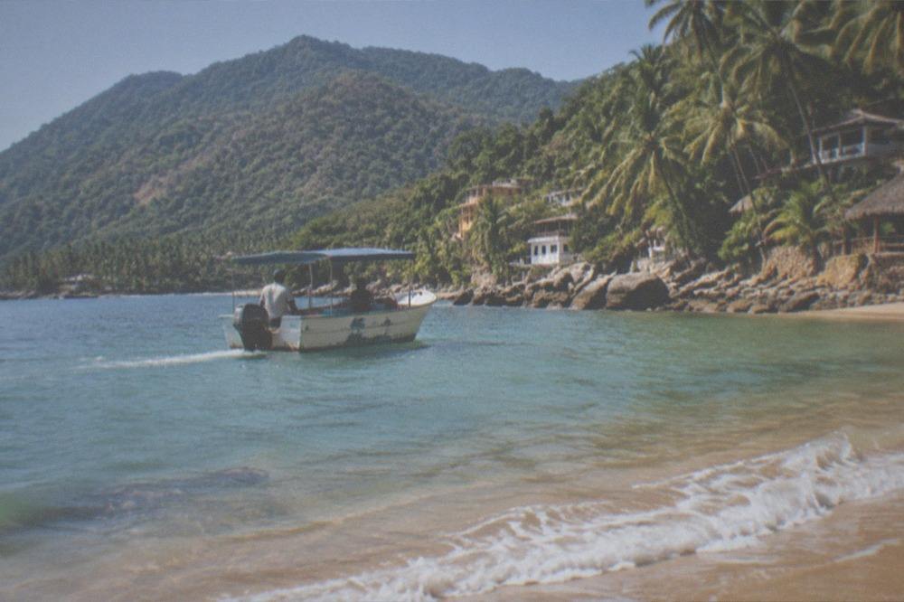 A wooden water taxi approaching a palm-lined beach cove at Yelapa