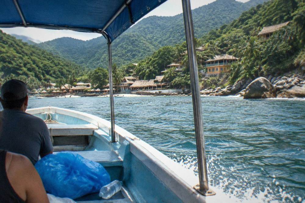 A covered passenger boat crossing open water toward a green mountainous coastline